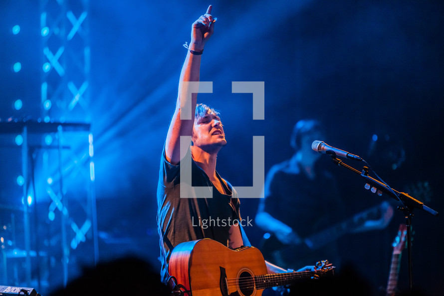 A musician on stage with arm raised lifted worship leader passion guitar pointing up finger