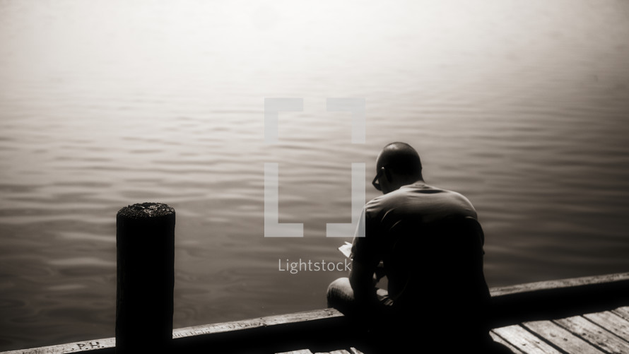 A man reading his Bible on the edge of a dock