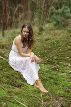 a young woman sitting on mossy ground alone in a forest 