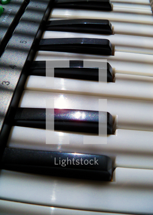 The black and white piano keys of an electronic keyboard / synthesizer being lit by afternoon  sunlight and shadows at a local church. 