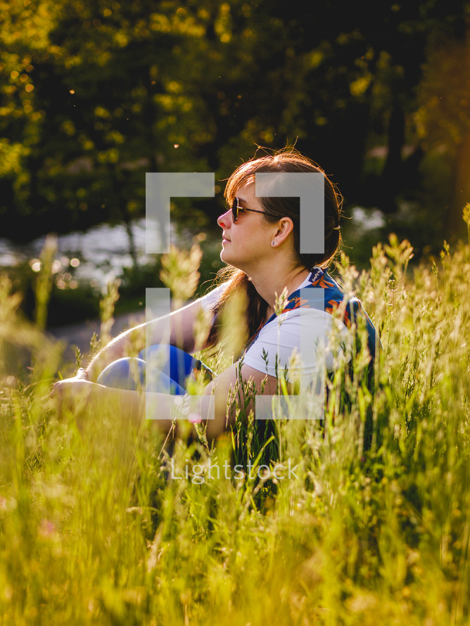 A woman sits amongst some grass looking into the distance