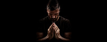 Portrait of a man praying over black background with copy space. Hands folded in prayer.