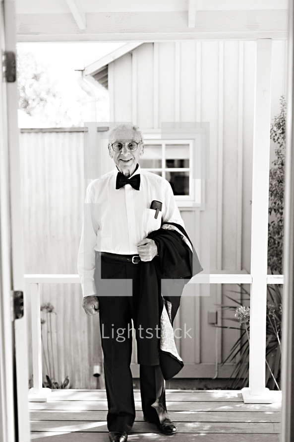 Elderly man in suit  smiling holding jacket in hand on porch tuxedo 