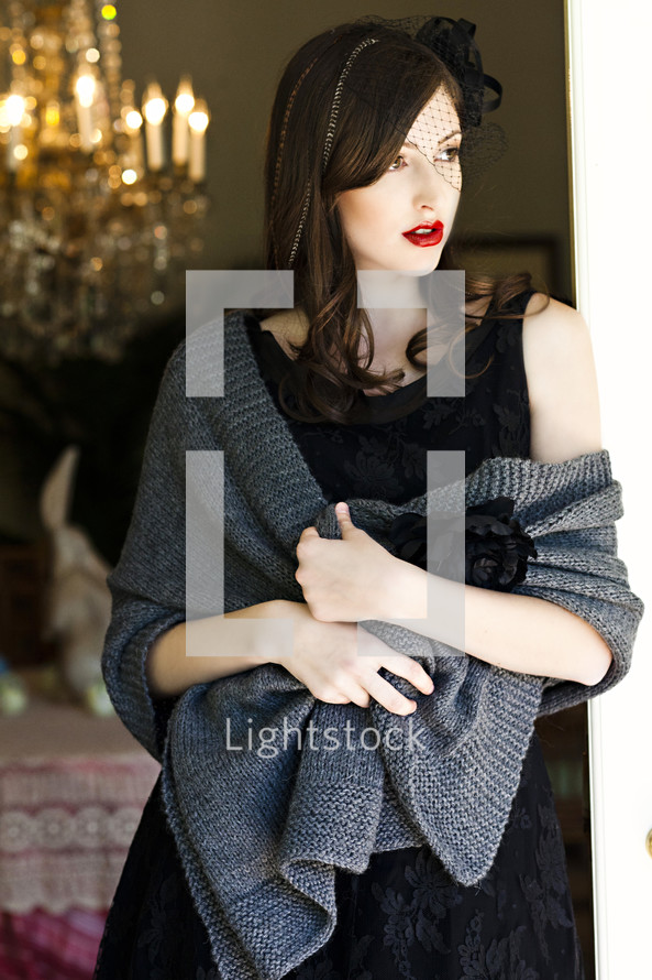 A young woman in a black dress wrapped in a shawl and leaning against a doorjamb vail model fashion
