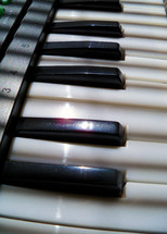 The black and white piano keys of an electronic keyboard / synthesizer being lit by afternoon  sunlight and shadows at a local church. 
