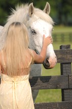girl in a yellow sundress petting the head of a white horse