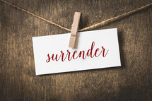 word surrender on white card stock hanging from a clothespin on a clothesline 