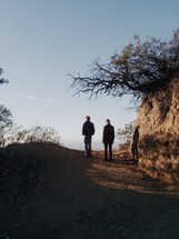 Two men walking on a dirt path. 