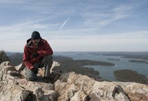 man kneeling in prayer on top of a mountain
