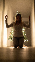 a woman kneeling in prayer in front of a Christmas tree 