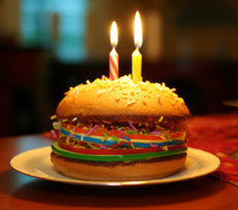 A close-up of a hamburger with a lit birthday candle, creating an unusual and playful birthday celebration