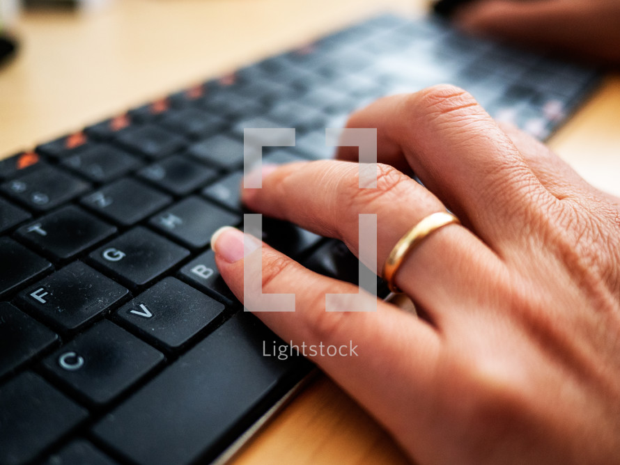 a woman's hand with wedding ring typing on a keyboard on a desk