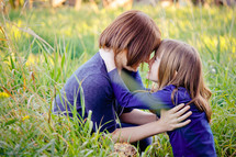 Mother and daughter embracing while sitting in a field of tall grass.