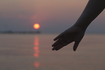 Womans hand silhouetted against a sunset