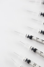 A line of hypodermic needles on a white background.