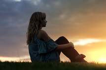 a woman sitting outdoors at sunset 