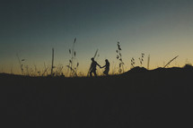 silhouette of a couple walking holding hands in a field at sunset