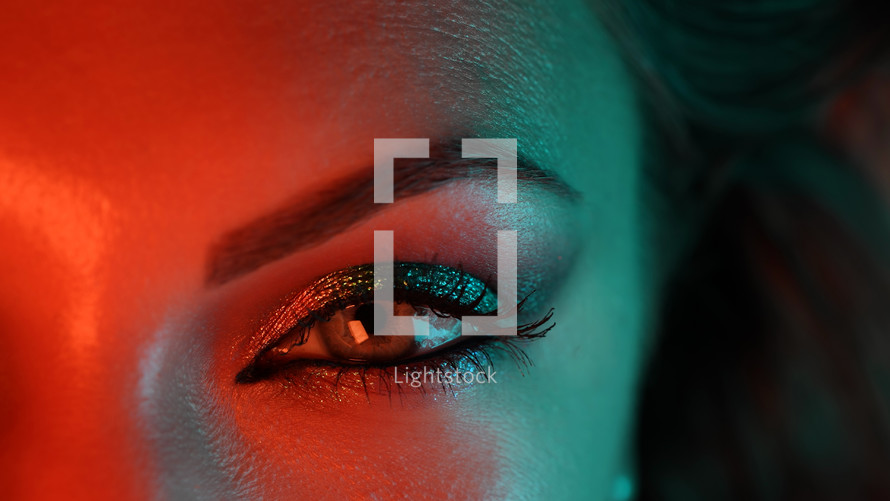 Close-up of woman eye under orange blue neon light. Female with beautiful makeup, glitter shadows. Beauty, cosmetics, night club lifestyle concept. High quality photo