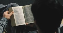 man sitting on the couch reading a Bible 