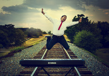 man jumping for joy on train tracks with a digital piano 