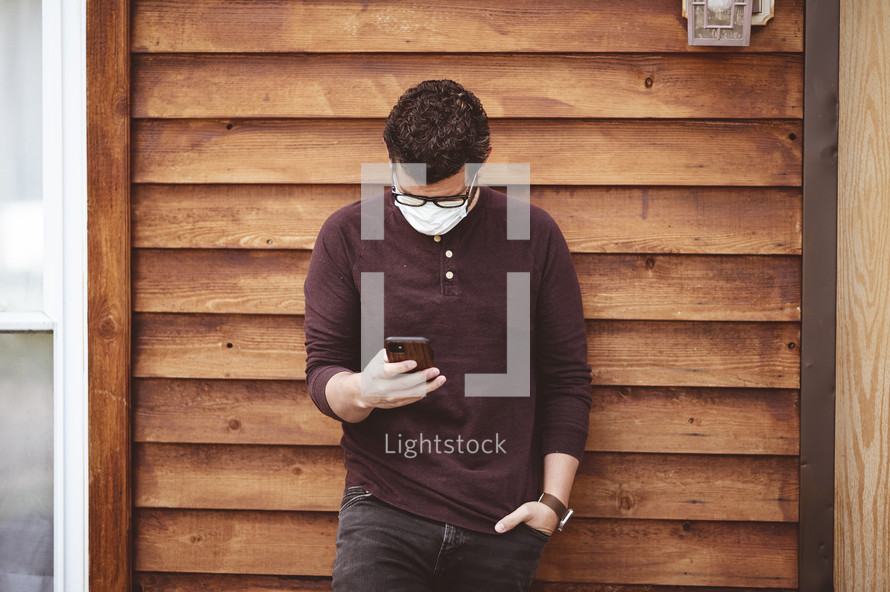 a man looking at his phone wearing a surgical mask 