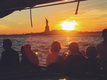 tourists on a ferry looking out at the statue of liberty at sunset