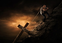 a man lifting a cross wrapped in a chain up a mountain 
