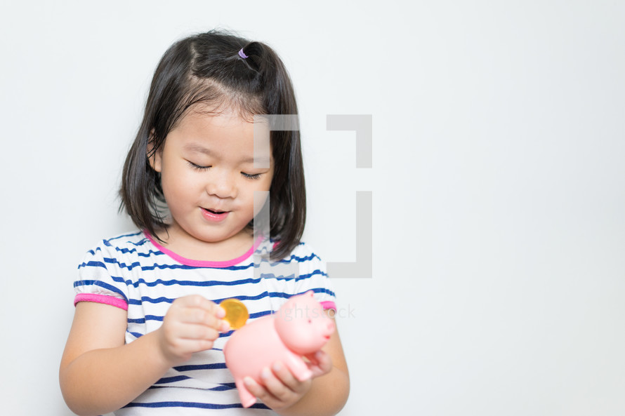  a little girl putting a coin in a piggy bank 