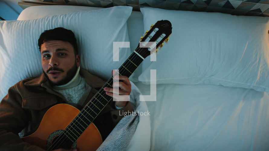 Man singing and playing the guitar in a bed