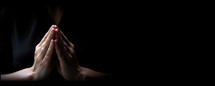 Hands of a woman praying on a dark background with copy space