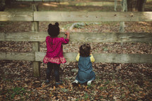 toddler girls looking through slates in a fence 