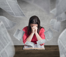 Woman praying while pages fly out of the Bible.