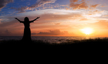 silhouette of a woman with arms raised in worship at sunset 