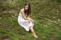 a young woman in dress siting on mossy ground 
