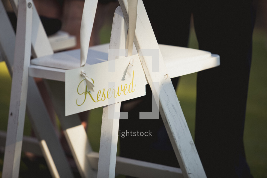 A reserved sign hanging on a white folding chair