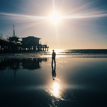 man near a pier on the beach walking on wet sand 