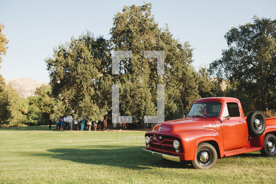 people gathered under a tree and an old vintage red truck