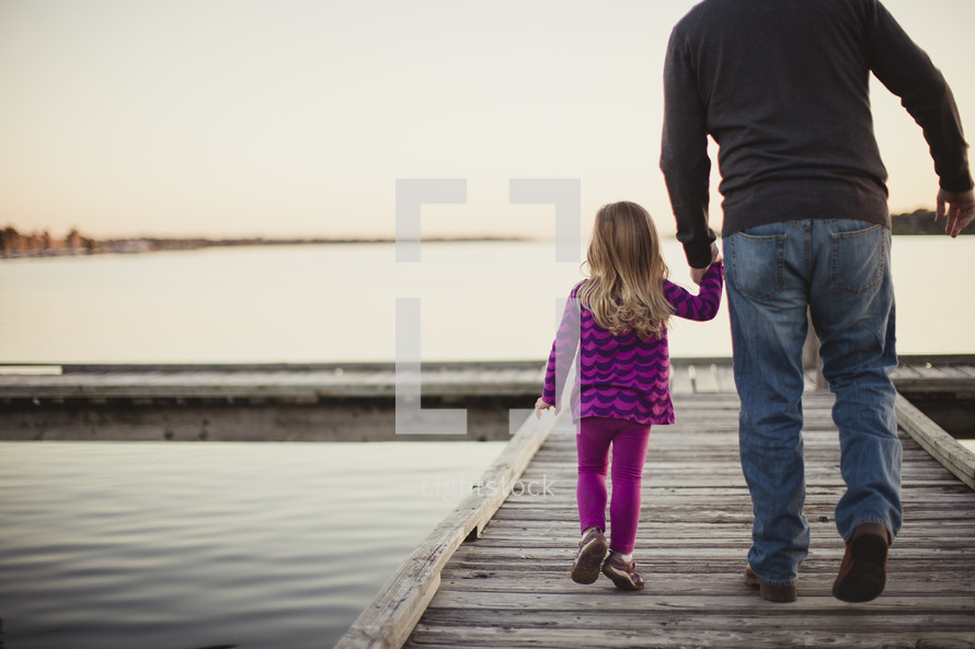 father holding hands with his daughter walking on a dock