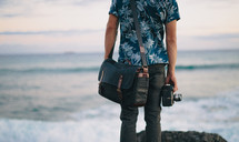 man in a Hawaiian shirt holding a camera looking out at the ocean 