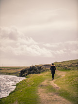 a woman walking on a path along a riverbank 
