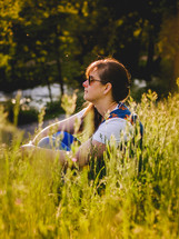 A woman sits amongst some grass looking into the distance
