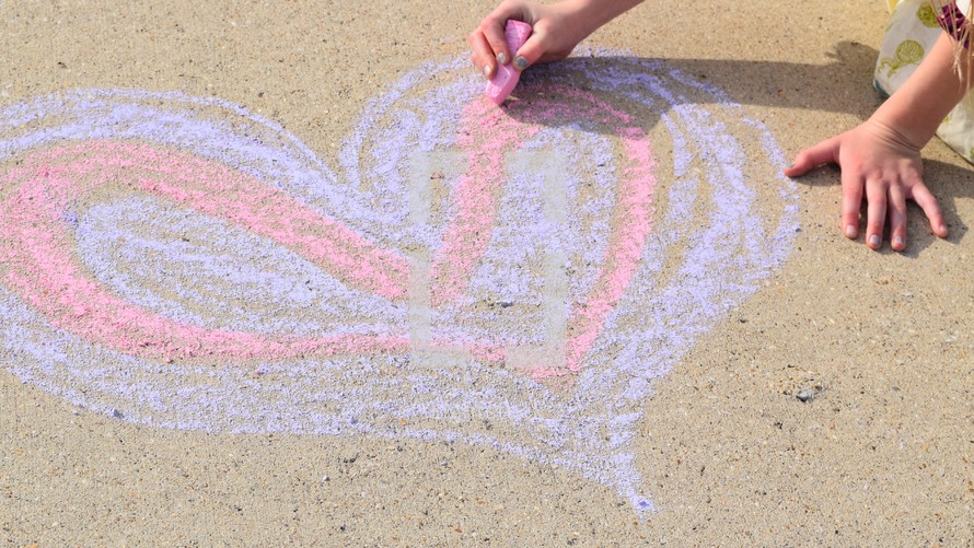 a little girl drawing a Valentine's purple and pink heart on concrete in sidewalk chalk 