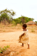 A small child walks barefoot in the dirt.