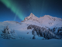 Aurora Borealis appear over a snow covered mountain in winter landscape. 