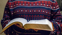 a woman reading a Bible in a sweater 