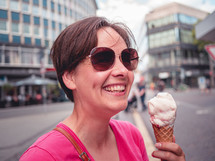 a woman smiles and laughs holding an ice-cream in the city
