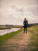 a woman walking on a path along a riverbank 