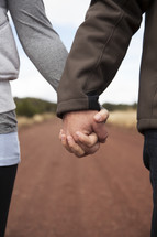 couple holding hands on a dirt road 