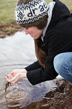 A woman scooping water in her hands from a stream.
