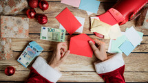 Santa Claus crafting envelopes with money as gifts 